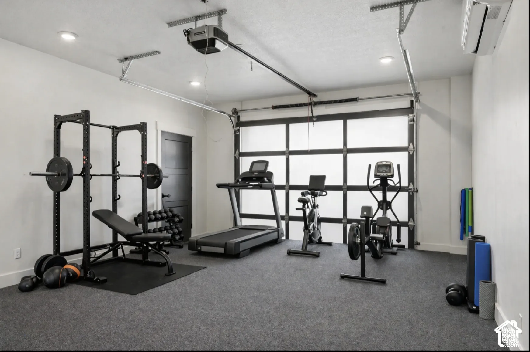 Finished garage space featuring a paneled glass sectional door, recessed lighting, wall-mounted climate control unit, and durable textured flooring