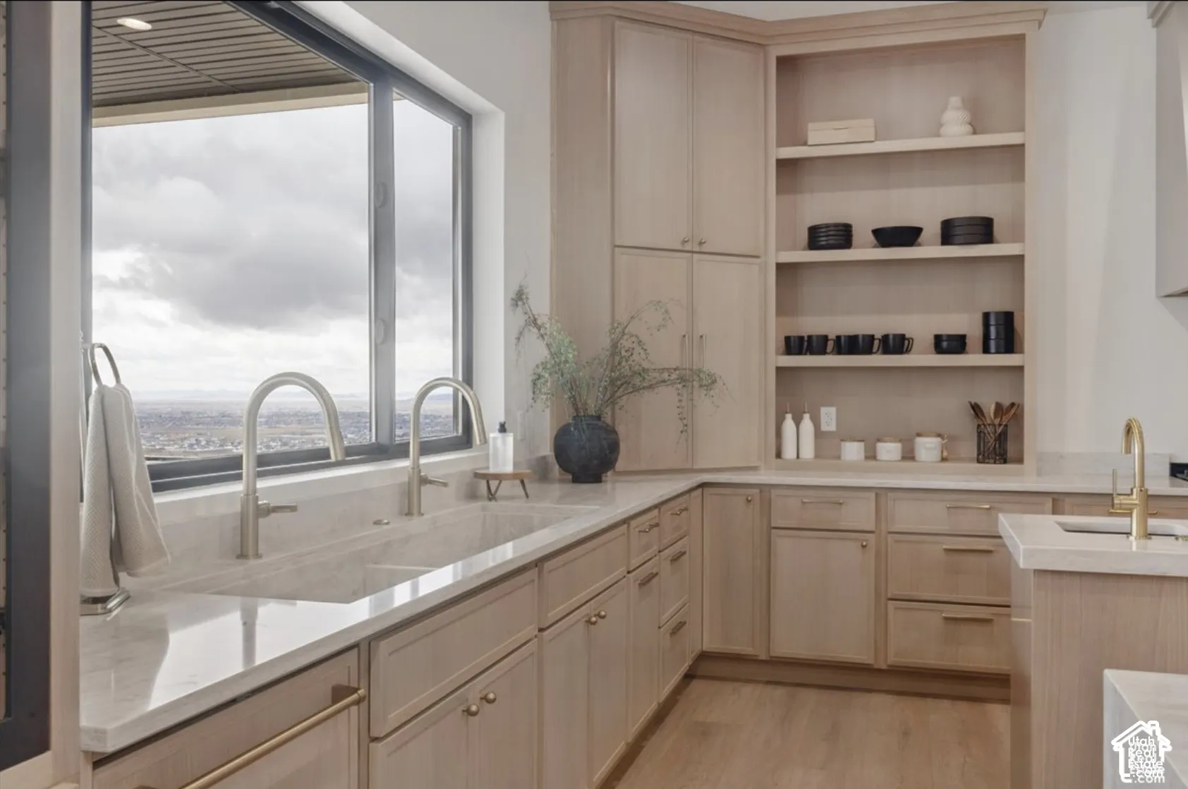 Custom light wood cabinetry, integrated open shelving, solid surface countertops, dual undermount sinks with arched brass faucets, and large windows