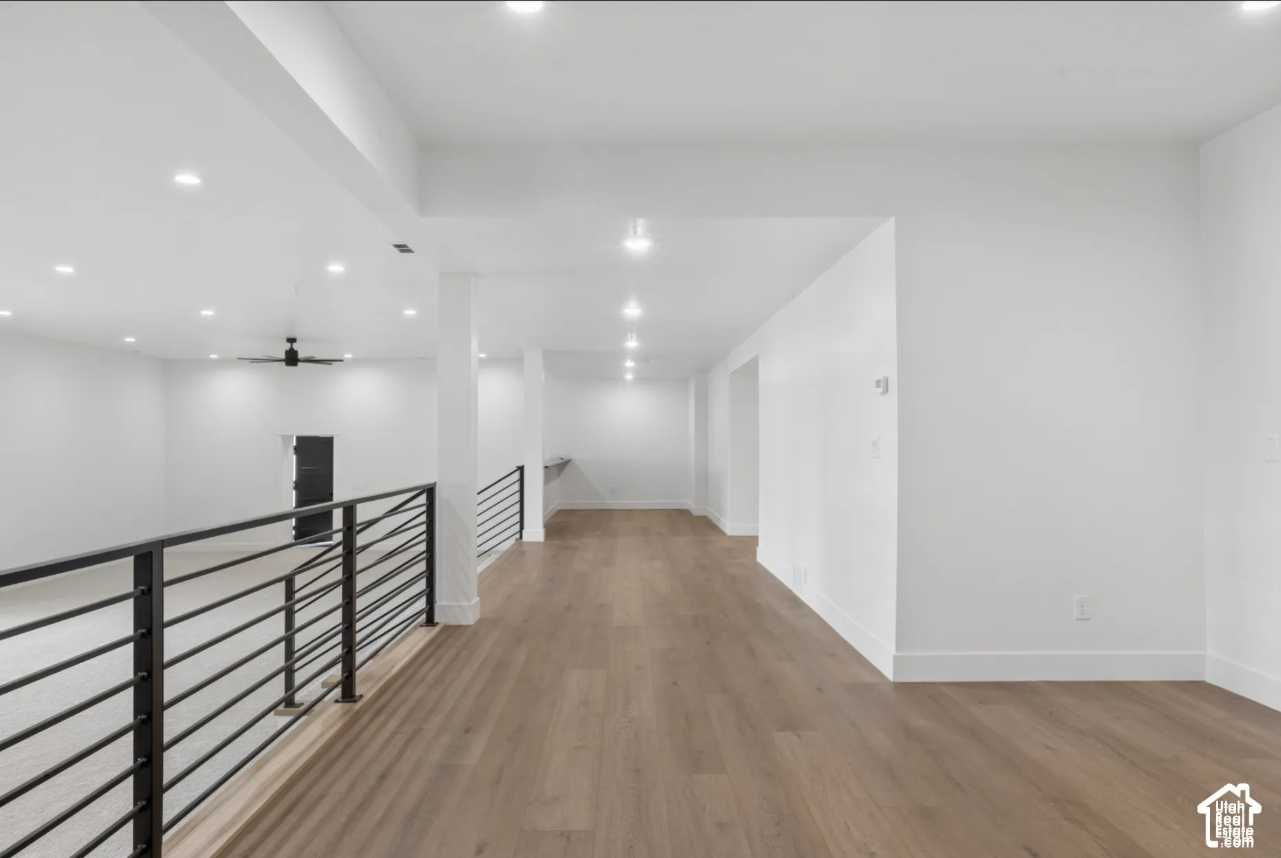 Open floor plan featuring wood-finish flooring, recessed lighting, and a metal horizontal-bar railing