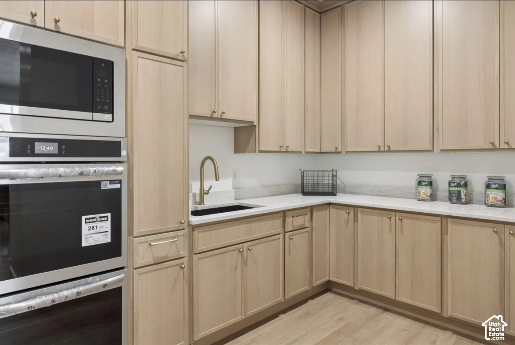 Light wood-finish cabinetry, quartz countertops, stainless steel double wall oven and microwave, undermount sink with brass-finish faucet, and wood-finish flooring