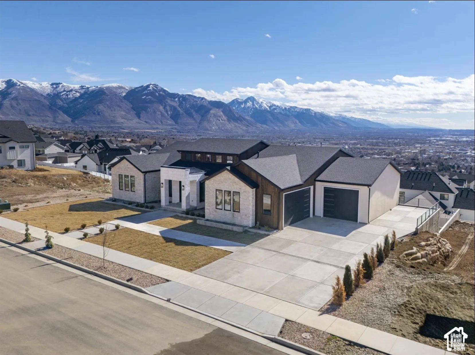Multi-level residence featuring a stone and siding exterior, expansive concrete driveway, three-car garage, and a backdrop of mountain peaks