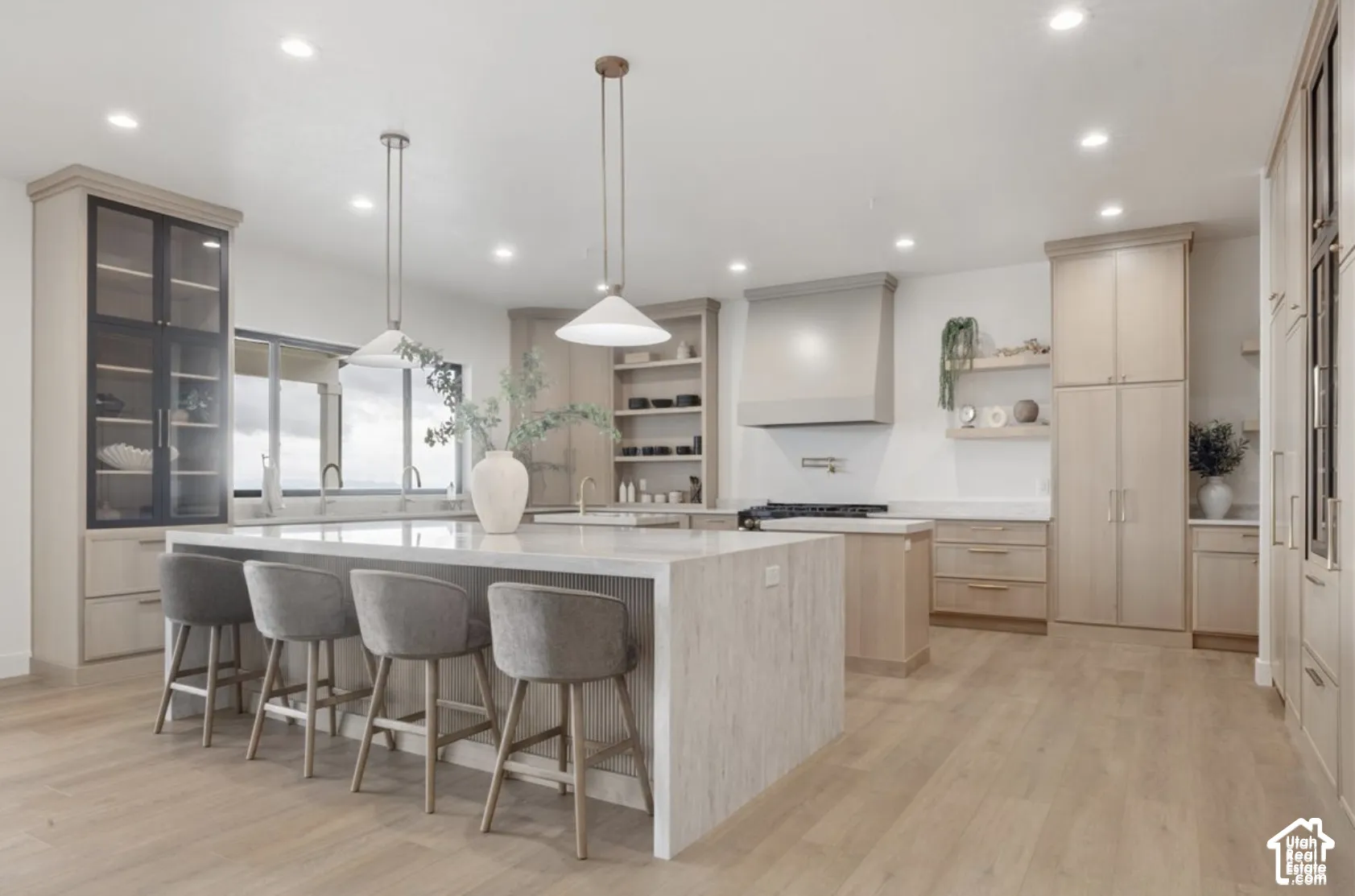 Gourmet kitchen featuring a waterfall-edge center island, light wood-finish cabinetry, built-in panel-ready appliances, dual pendant lighting, and recessed ceiling lights