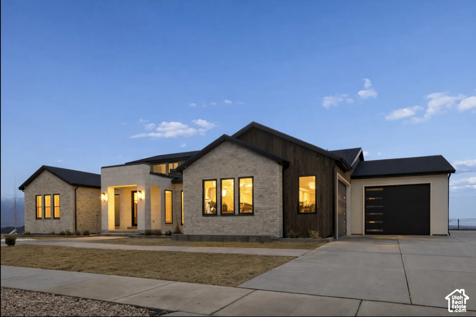 Contemporary exterior featuring a combination of light-toned stacked stone and vertical wood-finish siding, multi-gabled rooflines, large rectangular windows with dark frames, and an attached multi-car garage with modern horizontal panel doors