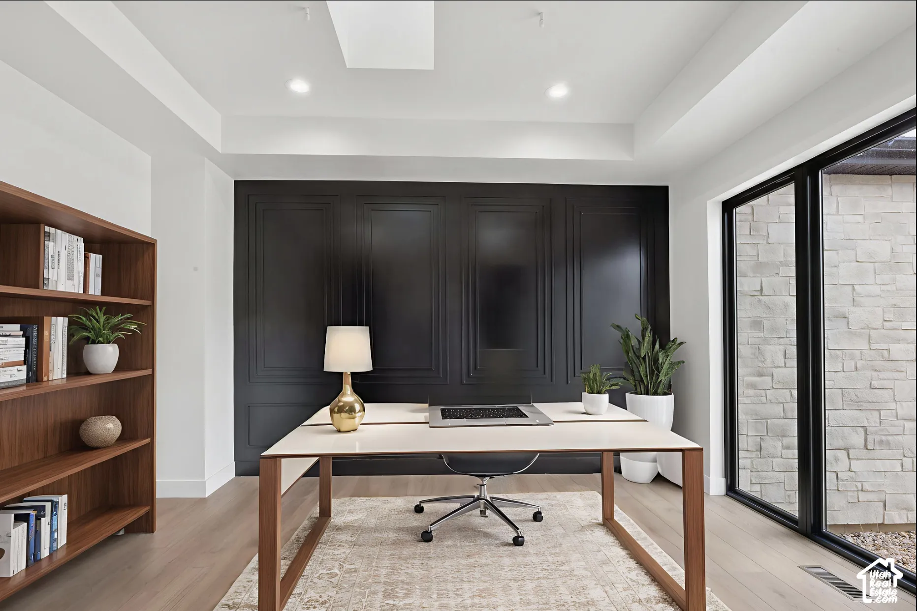 Black paneled accent wall, tray ceiling with recessed lighting, built-in wood shelving, wood-finish flooring, and floor-to-ceiling glass door featuring exterior stone masonry
