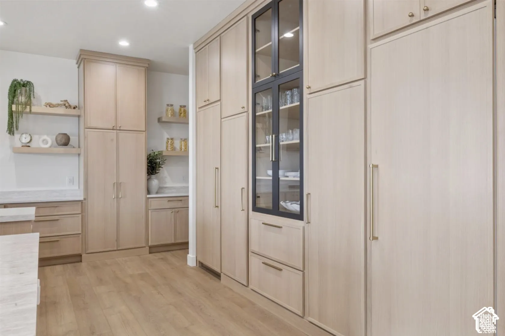 Floor-to-ceiling cabinetry with light wood finish, integrated glass-front display cabinet, matte gold hardware, recessed lighting, and floating shelving