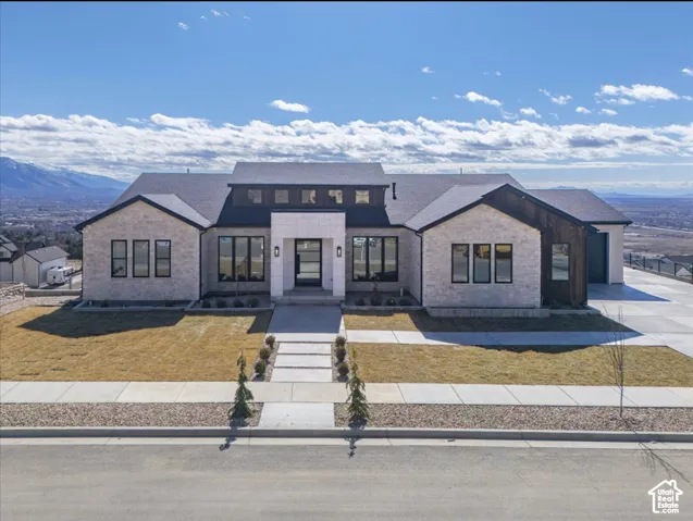 Single-story exterior featuring light stone masonry, vertical wood-panel siding, dark-frame windows, a prominent clerestory roofline, and an expansive concrete driveway