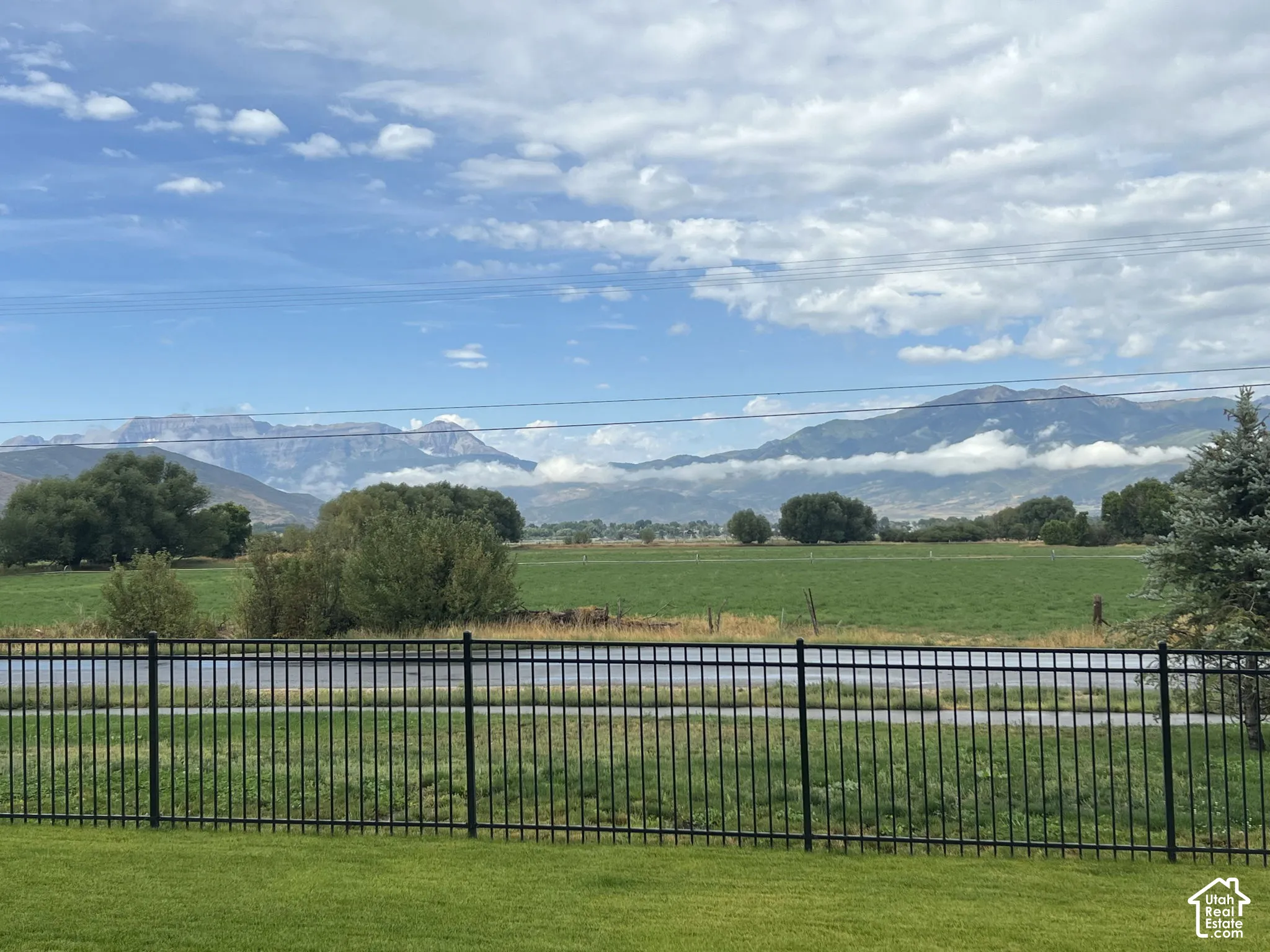 Black metal perimeter fencing enclosing a level lawn, featuring open fields and a mountain range backdrop