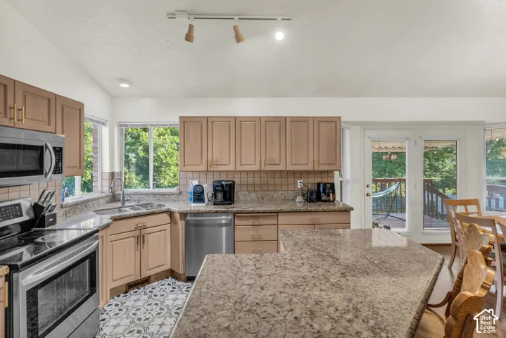Kitchen featuring an expansive stone-surface peninsula, stainless steel appliances, custom cabinetry, tiled backsplash, and recessed track lighting