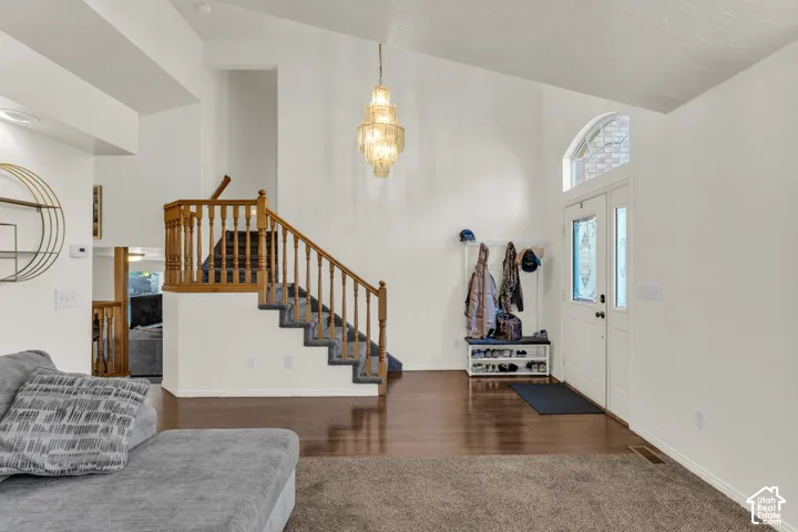 Entryway featuring vaulted ceilings, a multi-tiered chandelier, wood-finish flooring, a wood-railing staircase, and an arched transom window