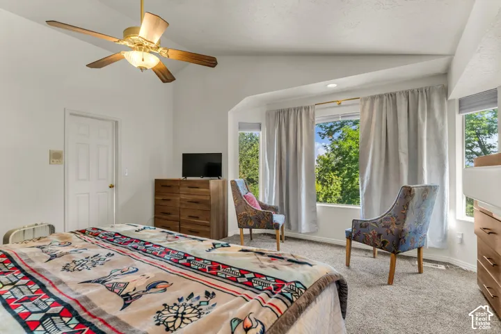 Vaulted ceiling featuring a central multi-blade ceiling fan, expansive windows, and wall-to-wall carpeting