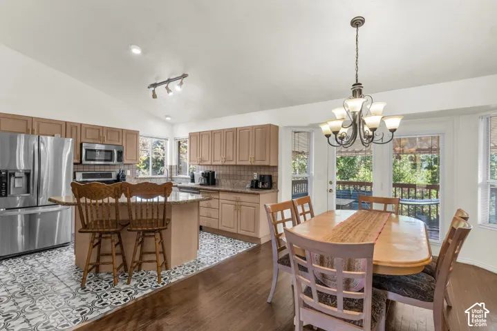 Kitchen featuring wood cabinetry, a central island with countertop seating, stainless steel appliances, patterned tile flooring, and a formal chandelier