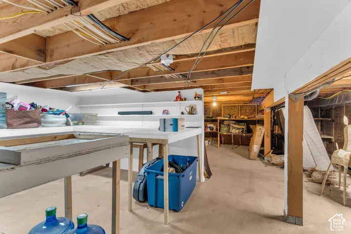 Unfinished storage space featuring a concrete floor, exposed wood ceiling joists, and fixed white shelving units