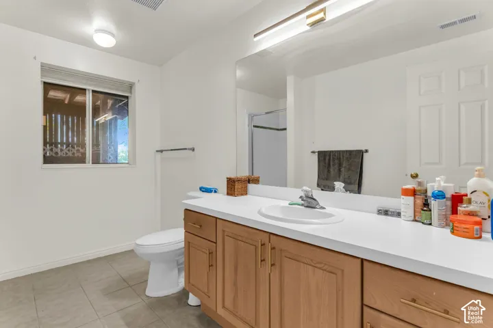 Bathroom featuring a wooden vanity with brass-finish hardware, a solid-surface countertop with an integrated oval sink, a full-width wall mirror, and neutral tile flooring