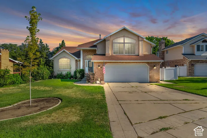 Split-level exterior featuring a brick and stucco facade, arched window detailing, an attached two-car garage, and a concrete driveway