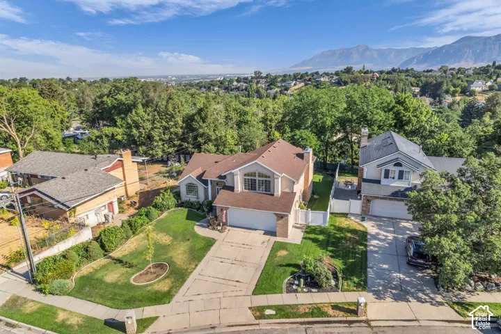 Two-story residence featuring a multi-gabled asphalt shingle roof, brick and stucco exterior, attached multi-car garage, and concrete driveway, set against a backdrop of mountain ranges and dense mature trees