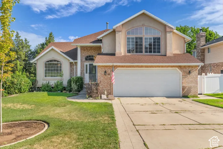 Two-story residence featuring a brick and stucco exterior, an attached two-car garage, and a gabled roofline with arched window detailing