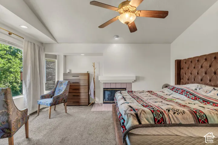 Vaulted ceiling featuring a central ceiling fan with integrated light fixture, carpeted flooring, and a fireplace with a ceramic tile surround and mantel