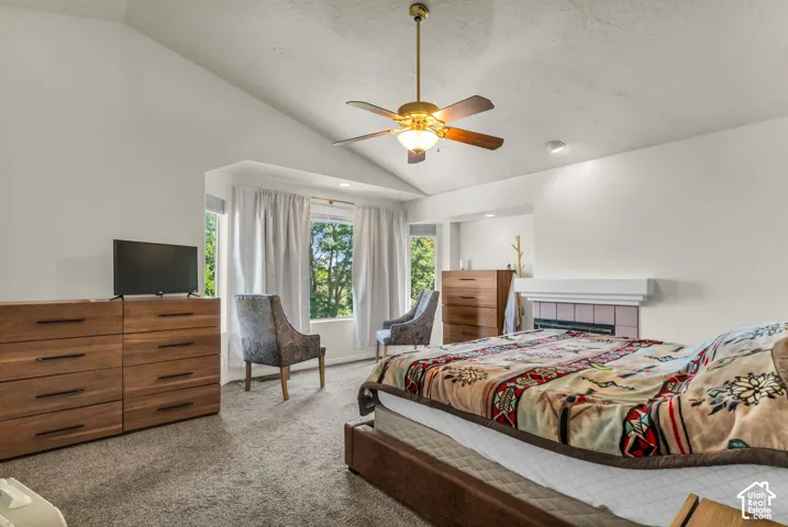 Vaulted ceilings, a built-in fireplace with a tile surround, a central ceiling fan, and large windows