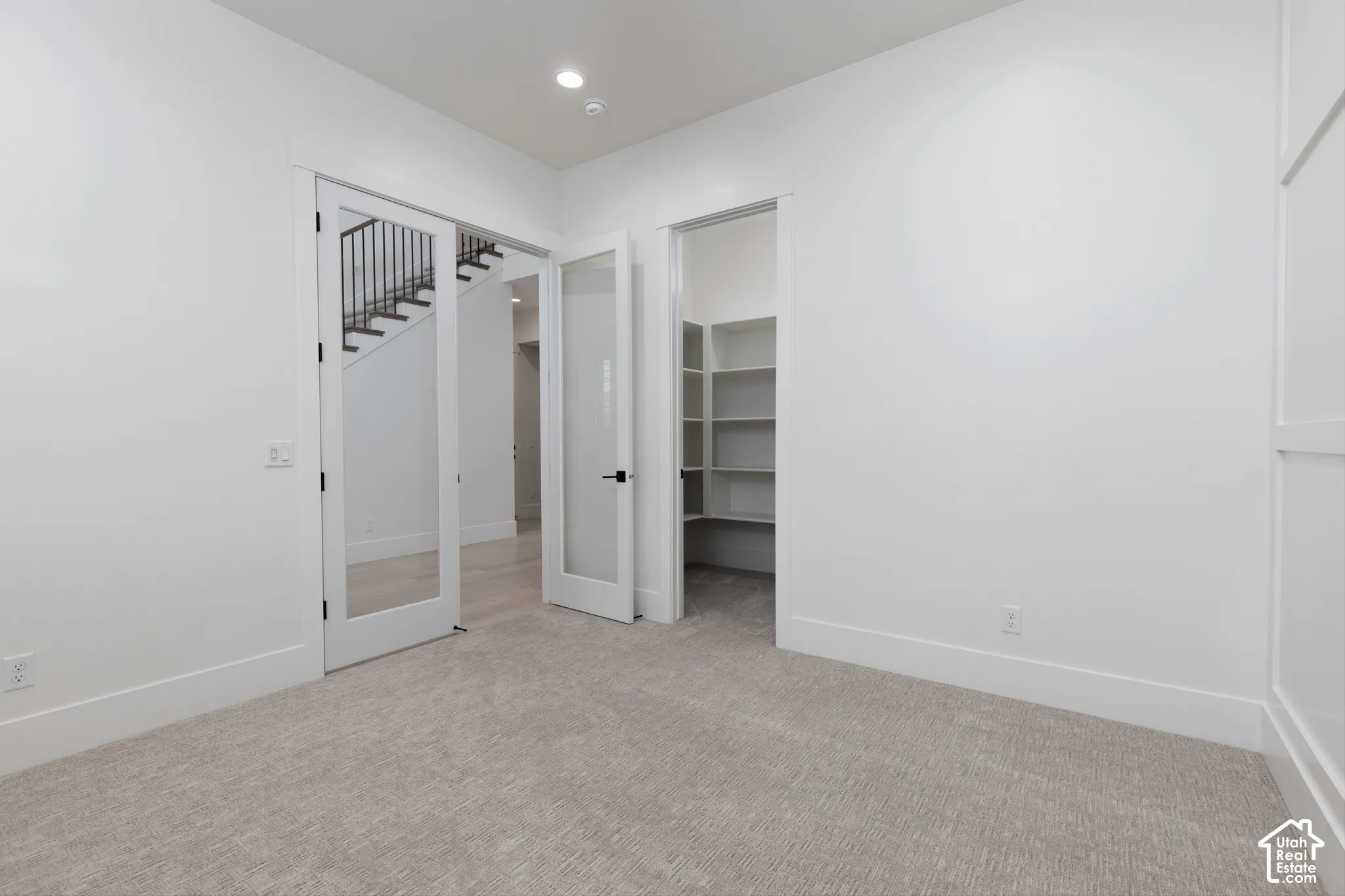 Room featuring wall molding, carpeted flooring, two glass-paneled doors, and an walk-in storage area with built-in shelving