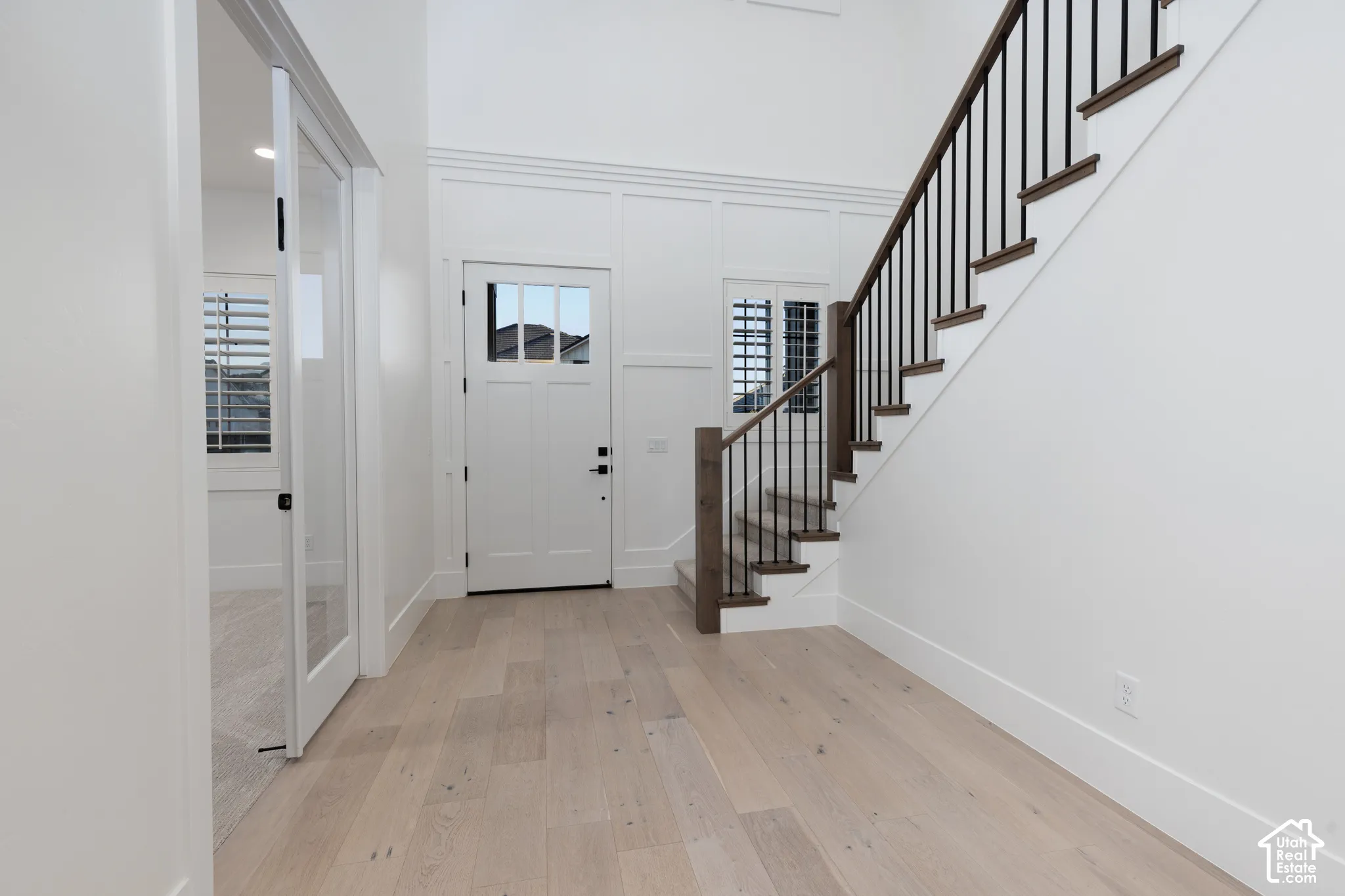 Entryway featuring wood-finish flooring, high ceilings, custom millwork wall paneling, and a staircase with stained wood handrails and metal balusters
