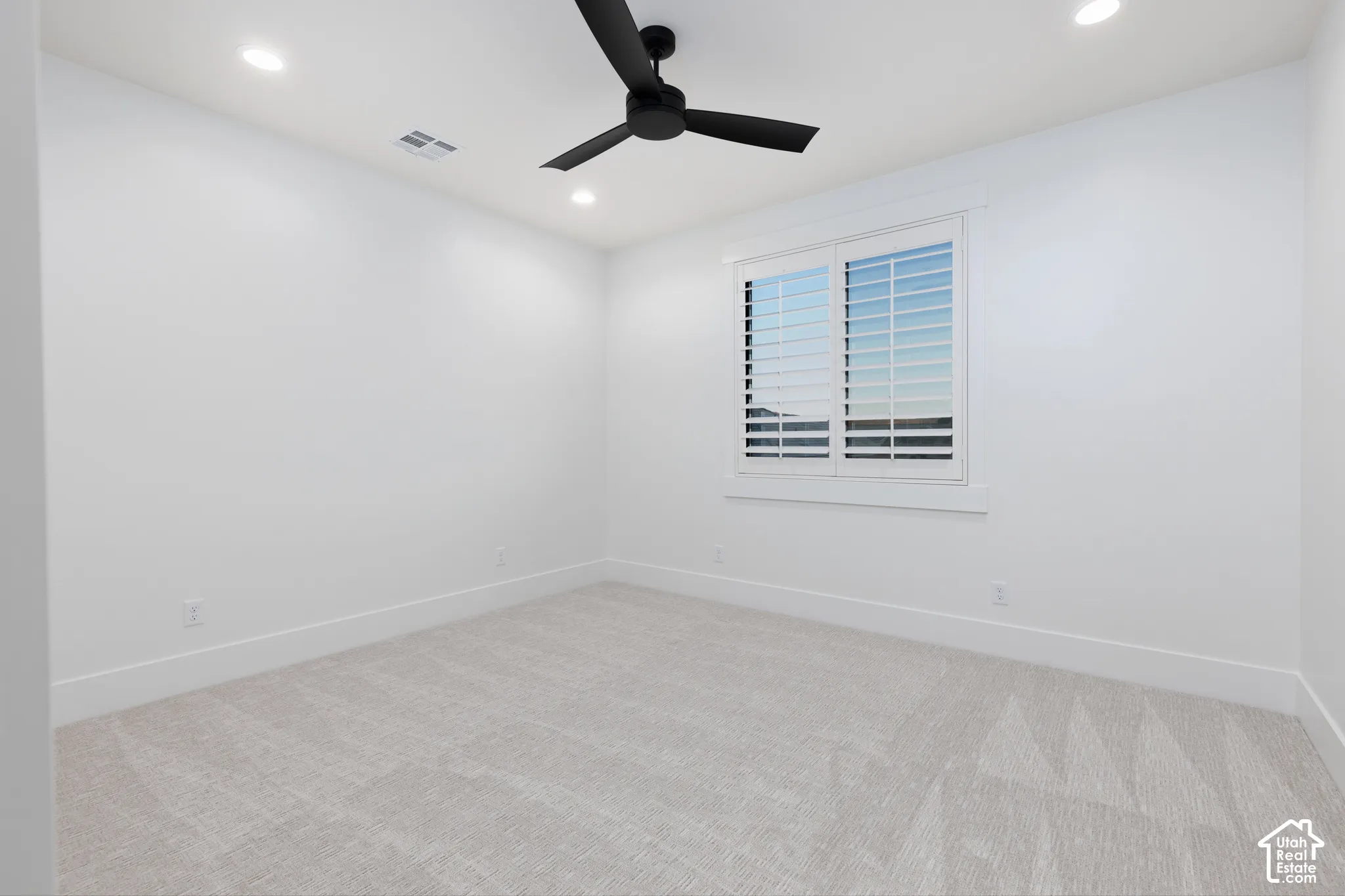 Neutral-toned carpeting, matte black ceiling fan, recessed lighting, and white plantation shutters