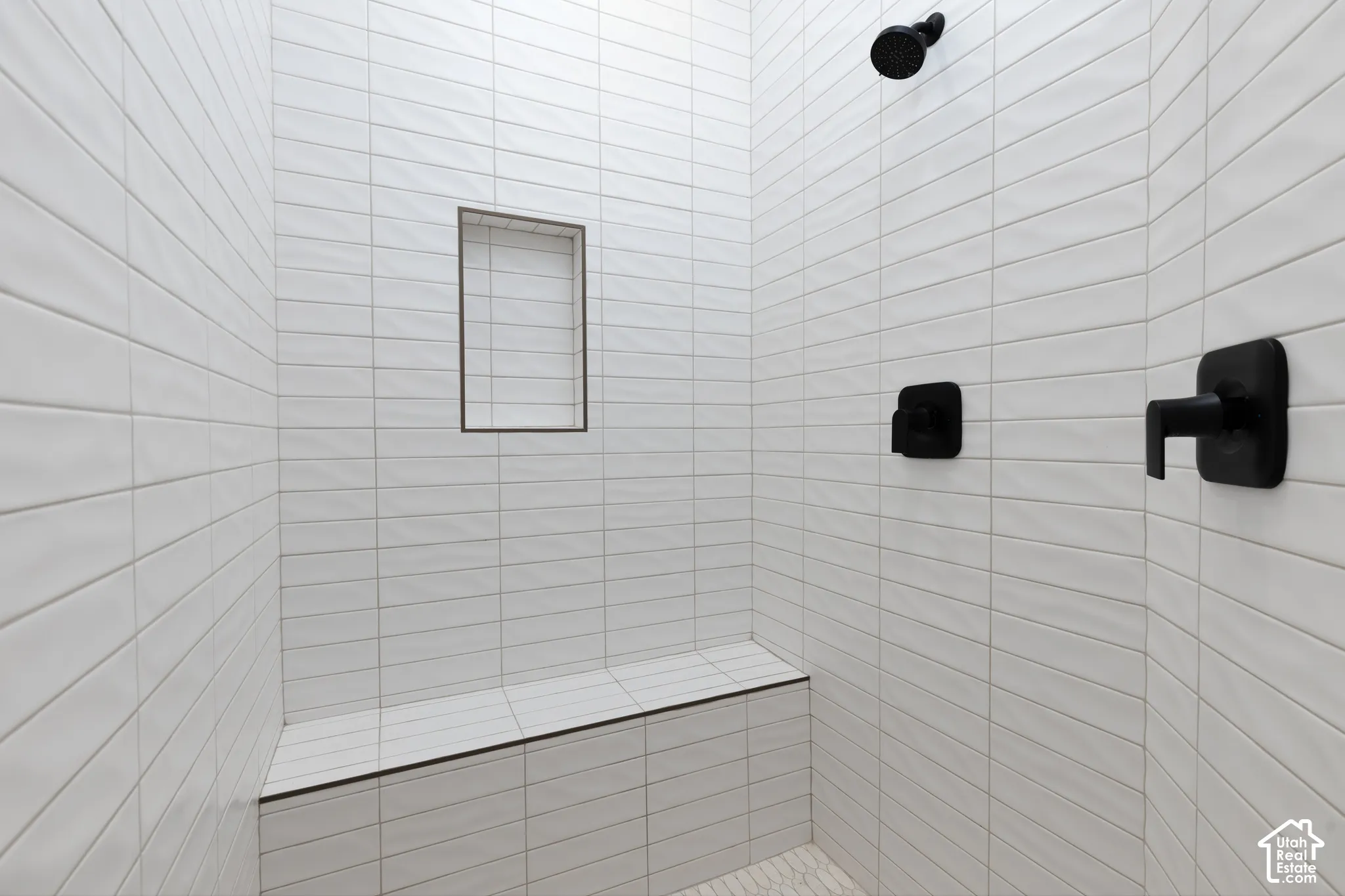 Shower stall featuring floor-to-ceiling white subway tile, built-in tile bench, recessed wall niche, and matte black plumbing fixtures