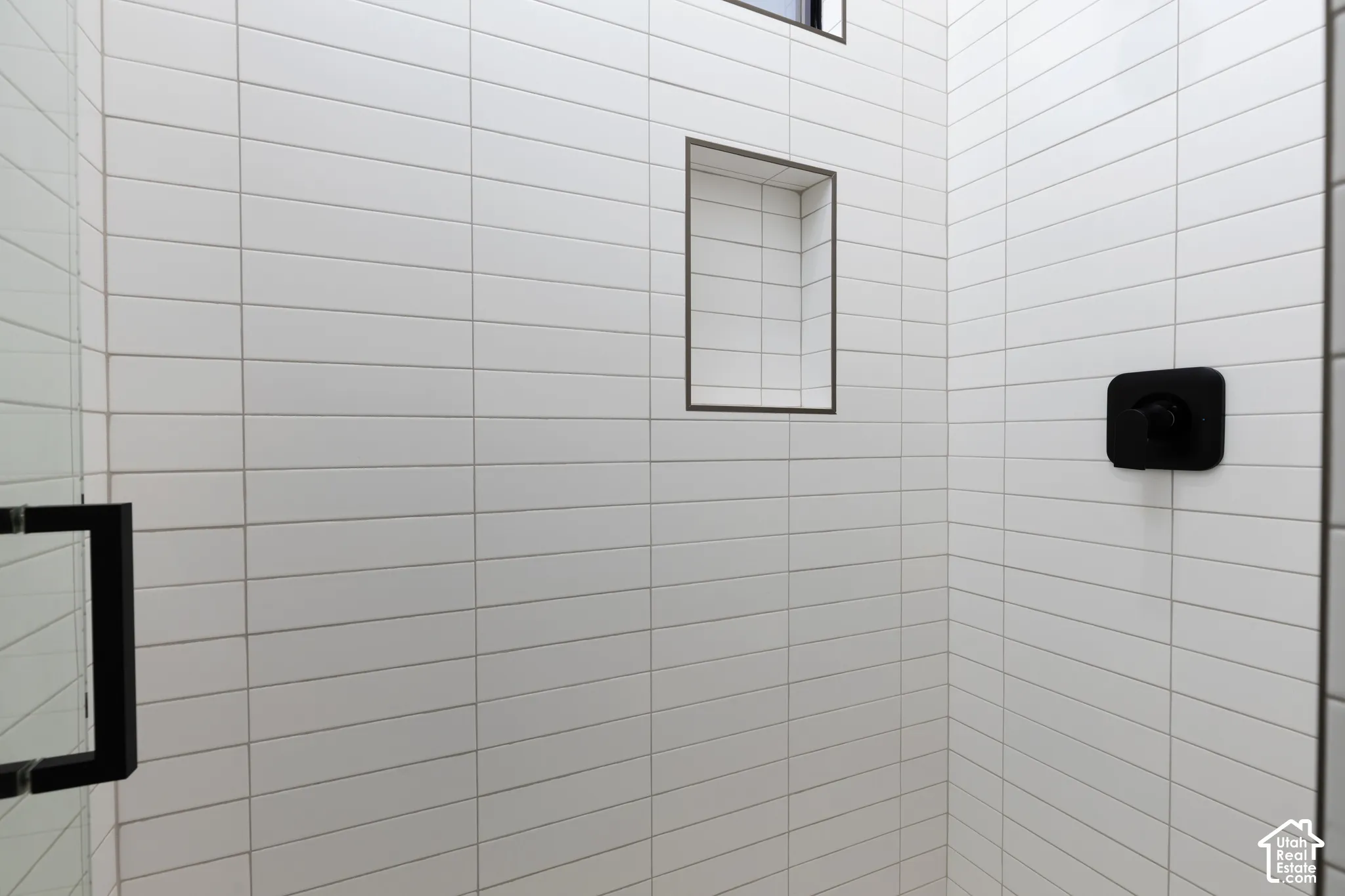 Shower featuring white elongated rectangular wall tile, built-in recessed shelving, matte black fixtures, and a frameless glass enclosure