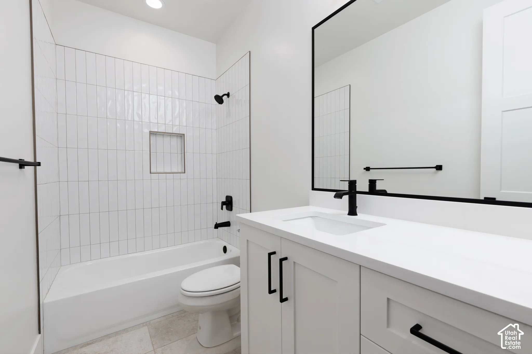 Bathroom featuring a white vanity with quartz countertop, matte black fixtures, vertical subway tile tub surround with built-in niche, and a framed vanity mirror