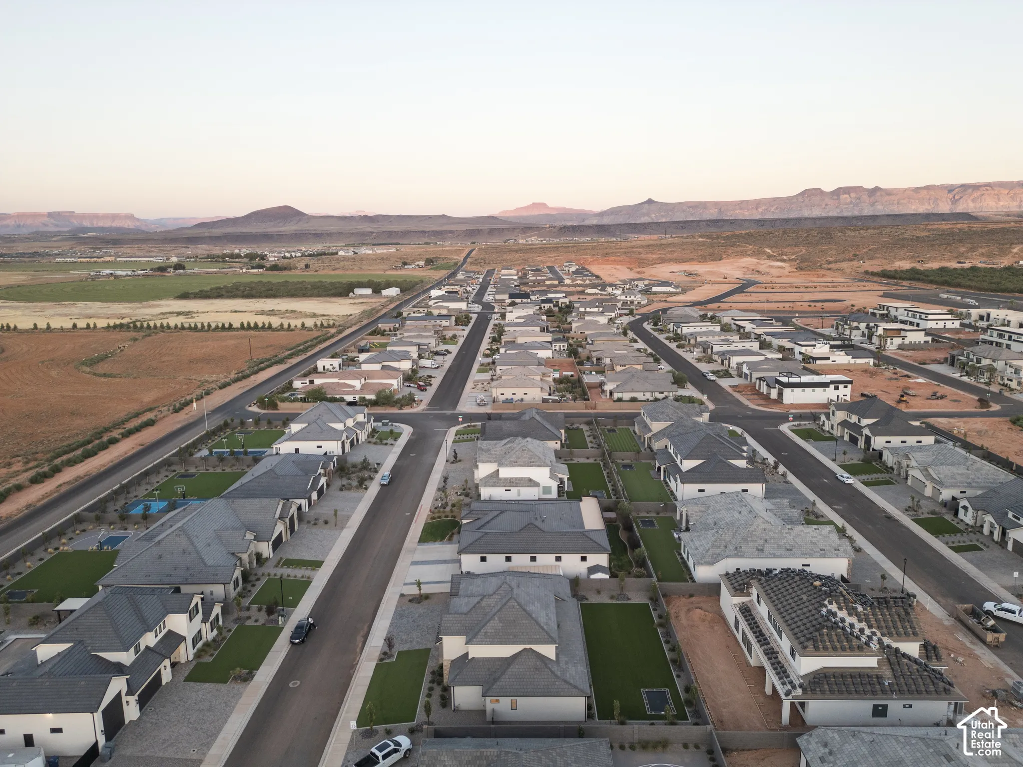 Aerial perspective of a suburban neighborhood featuring paved streets, established residential lots, manicured green lawns, and a prominent mountain range backdrop