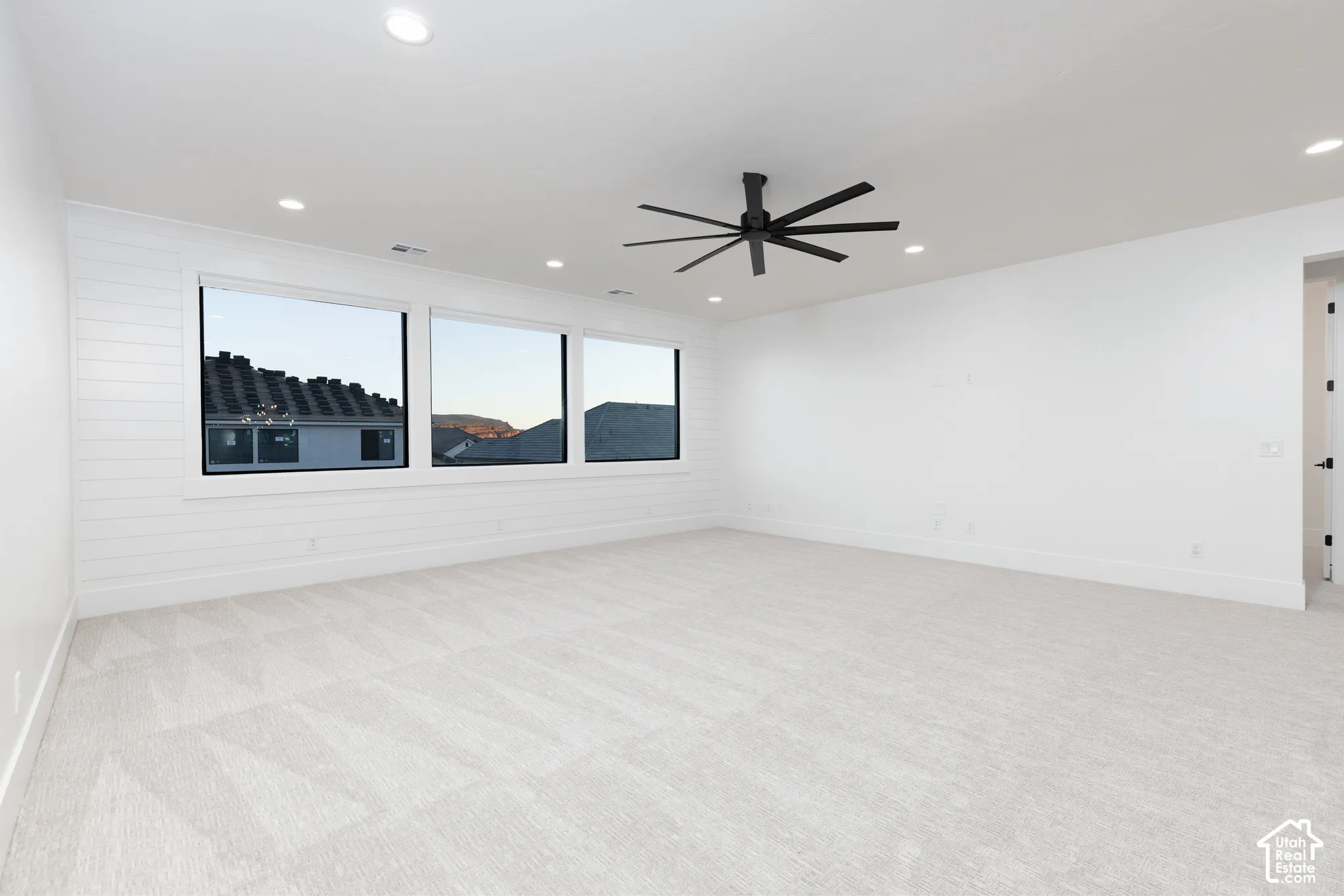 Expansive room featuring shiplap accent wall, triple-pane windows, recessed ceiling lighting, and a multi-blade ceiling fan