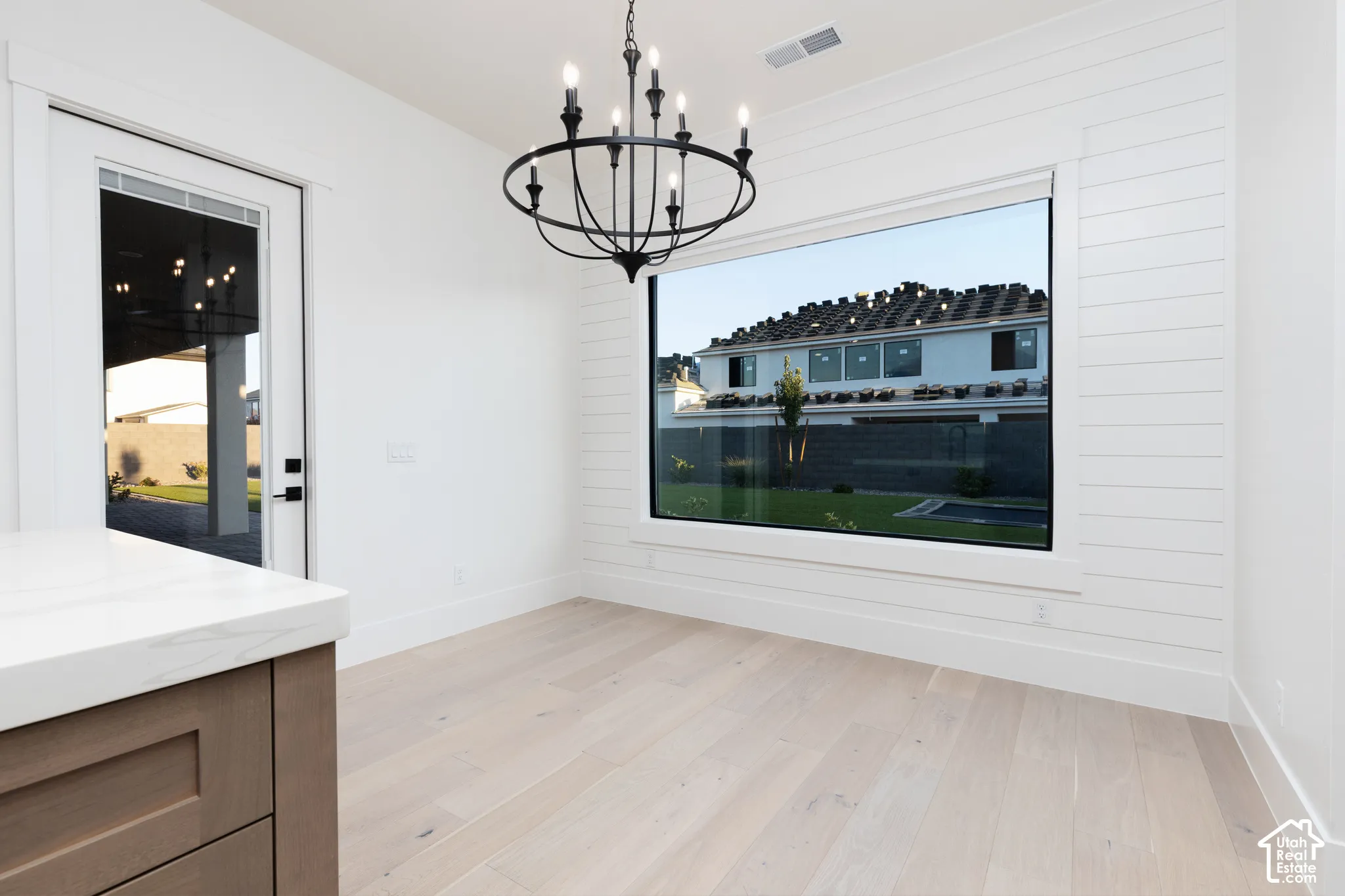 Wide-plank wood-finish flooring, horizontal shiplap wall detailing, large picture window, and a matte black multi-arm chandelier