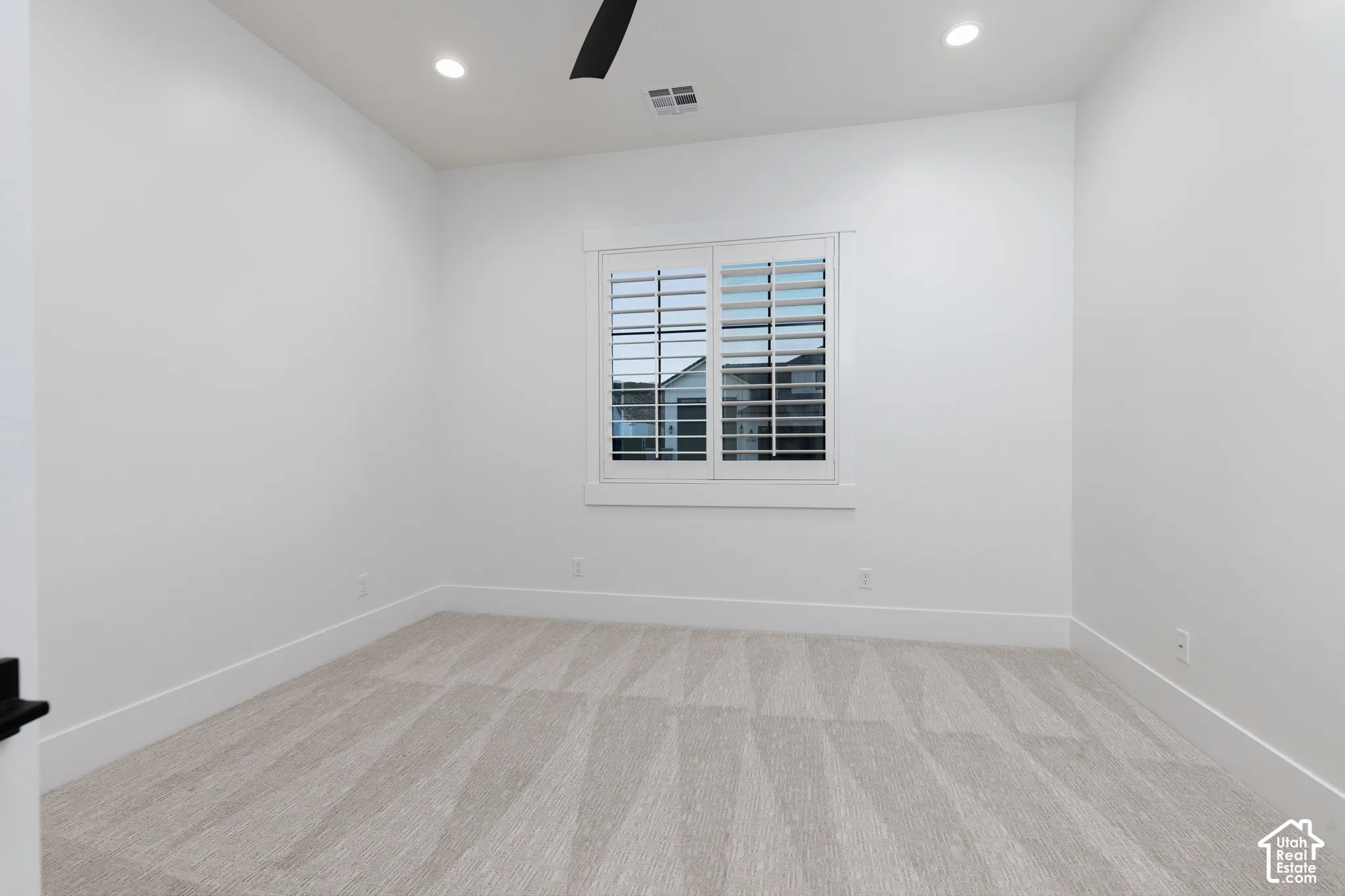 Neutral-toned carpeting, plantation shutters, recessed lighting, and a dark-finish ceiling fan