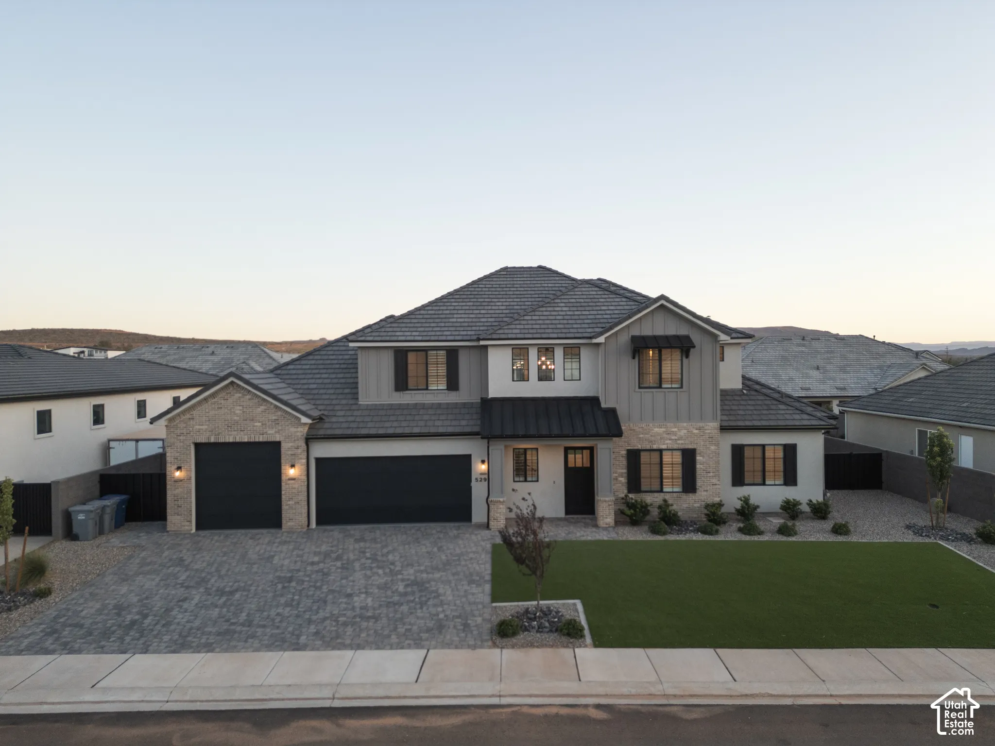 Two-story exterior featuring a stone and siding facade, tile roof, paver driveway, three-car garage, and metal awning accents