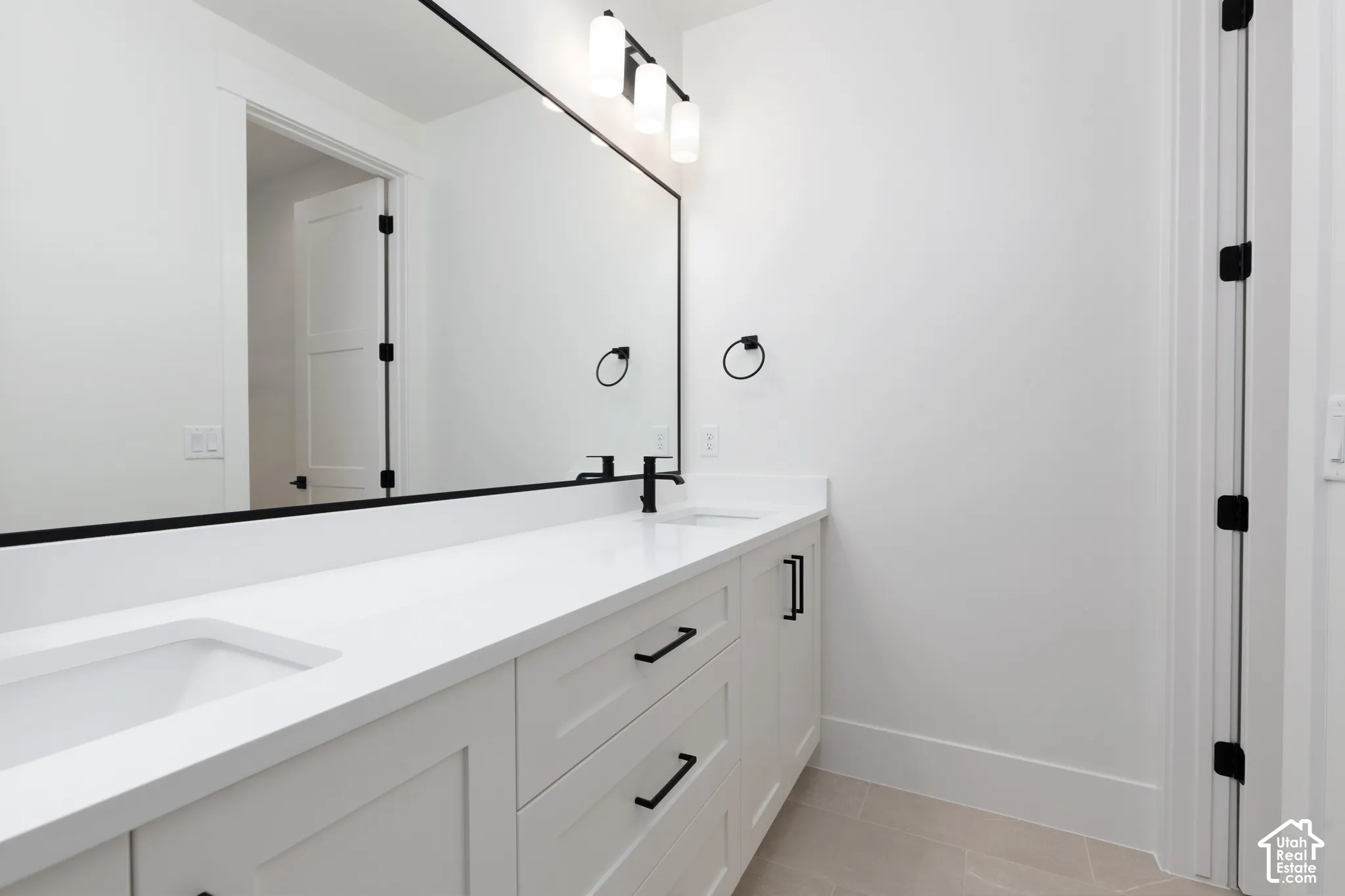 Dual-sink vanity featuring a white quartz countertop, matte black hardware, large-format mirror with a black frame, and wall-mounted light fixtures
