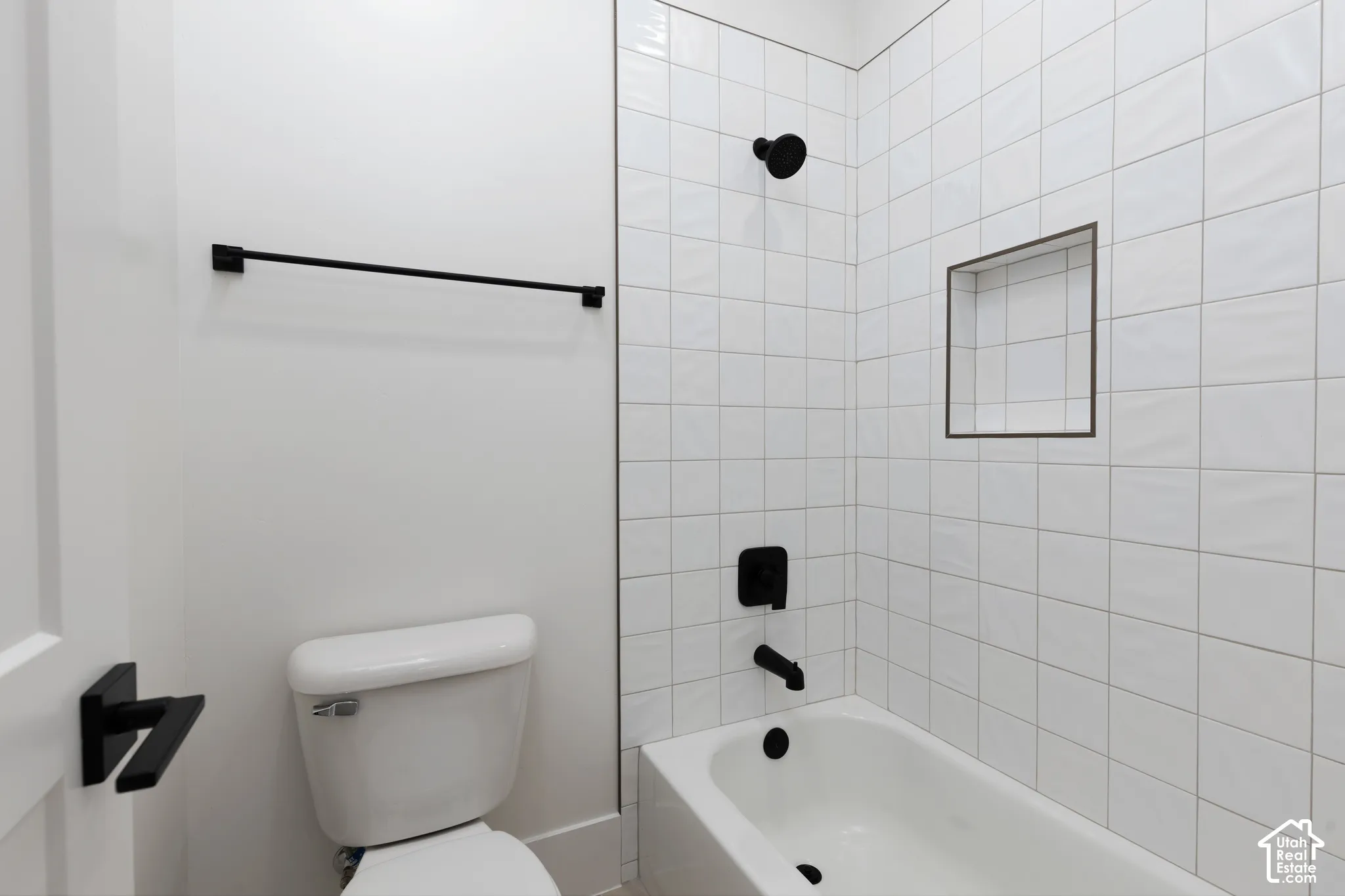 Full-height white square wall tiling, built-in recessed shower niche, matte black faucet and shower head hardware, and a matching matte black towel bar