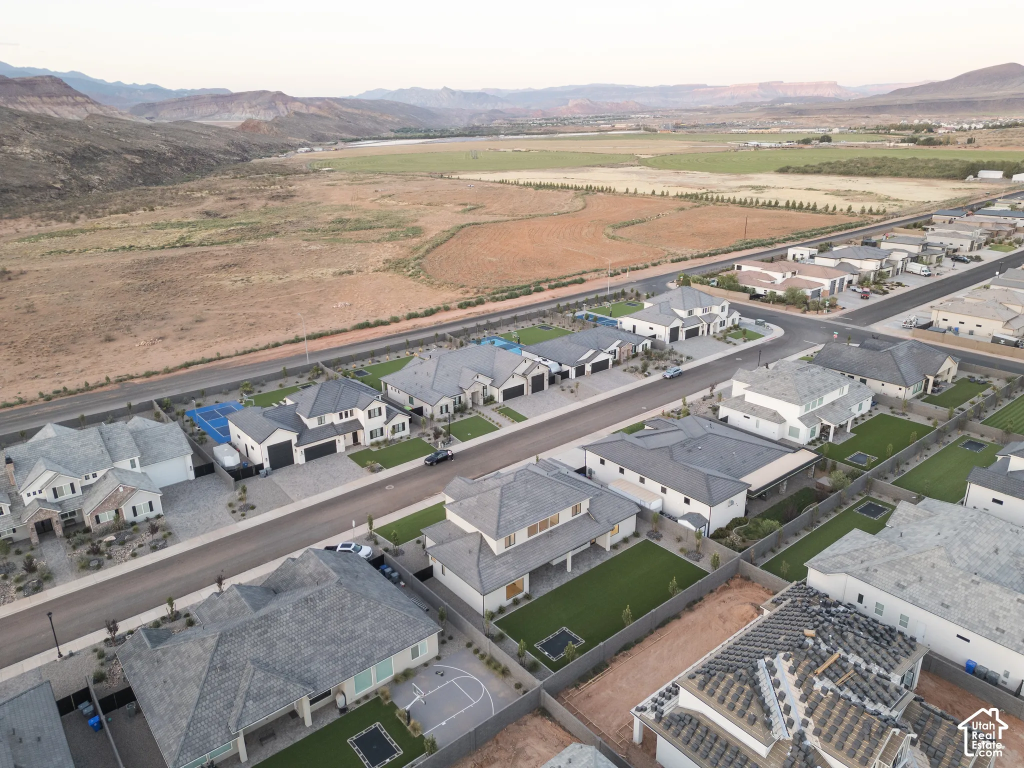 Aerial perspective of a suburban community featuring paved roads, uniform residential dwellings, fenced backyards, and expansive mountain scenery