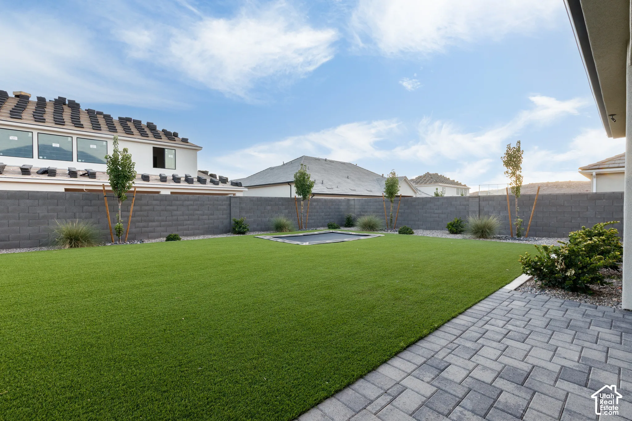 Private backyard featuring synthetic turf, paver patio, masonry perimeter wall, and in-ground trampoline