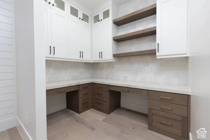 Built-in cabinetry featuring white upper cabinets with glass-paneled doors, wood-finish lower drawers, stone-surface countertops, square tile backsplash, and floating wood shelving