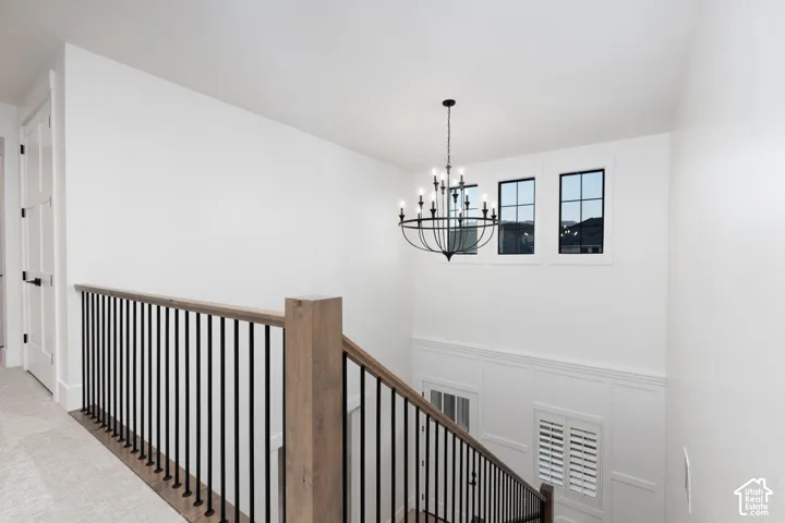 Staircase featuring a wood handrail, metal balusters, a multi-light chandelier, paneled wall detailing, and multi-pane windows