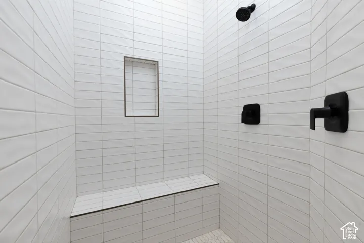 Shower stall featuring floor-to-ceiling white subway tile, built-in tile bench, recessed wall niche, and matte black plumbing fixtures