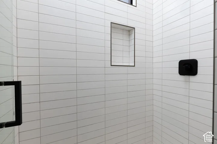 Shower featuring white elongated rectangular wall tile, built-in recessed shelving, matte black fixtures, and a frameless glass enclosure