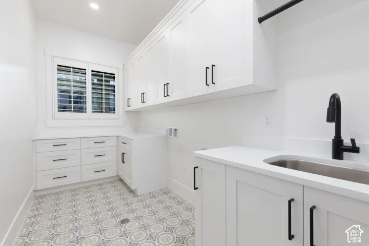 Utility room featuring white shaker-style cabinetry, quartz countertops, patterned tile flooring, an undermount stainless steel sink with a matte black faucet, and built-in hanging rod