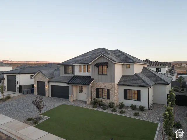 Exterior featuring a multi-gabled roofline, stone veneer accents, vertical siding, an attached three-car garage, and a paved driveway