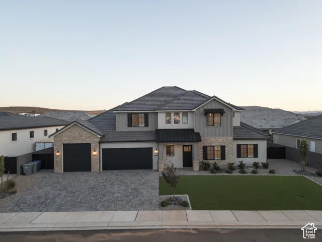 Two-story exterior featuring a stone and siding facade, tile roof, paver driveway, three-car garage, and metal awning accents