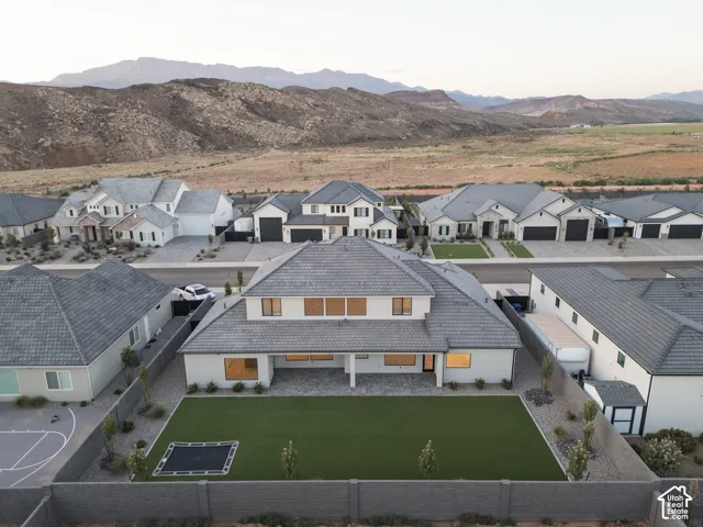 Two-story residence featuring a tile roof, covered rear patio, expansive synthetic turf lawn, stone-paved hardscaping, and perimeter masonry fencing, set against a mountain backdrop