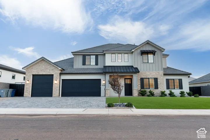 Multi-gabled exterior featuring stone veneer and vertical siding, dark metal roof accents, three-car garage, and paved driveway
