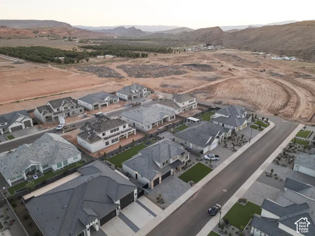 Aerial perspective of a suburban neighborhood featuring single-story residences with pitched shingle roofs, multi-car garages, paved driveways, and mountain scenery