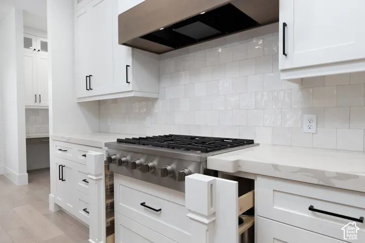 Kitchen featuring white shaker-style cabinetry, matte black hardware, stone countertops, a stainless steel gas range, and a tile backsplash