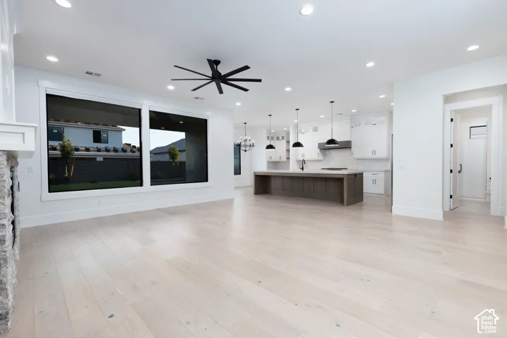 Open-concept interior featuring light wood-finish flooring, a kitchen island with a dark wood-finish base, stone fireplace surround, recessed ceiling lighting, and large picture windows