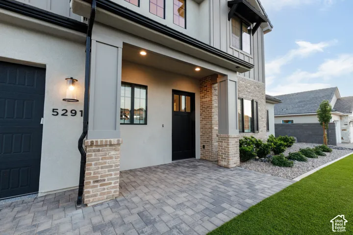 Exterior facade featuring a combination of stucco and masonry, covered entryway with paver flooring, modern panel door, and low-maintenance xeriscaped front yard